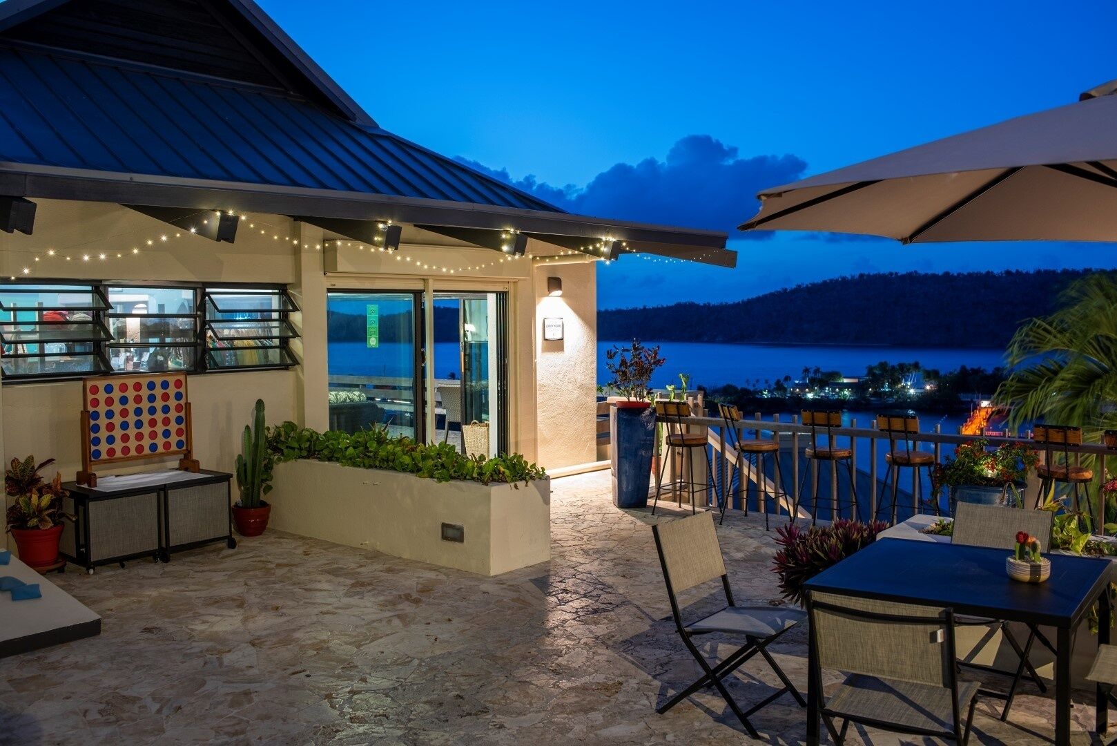 Eine Terrasse mit Blick auf einen See im Abenddämmerung, mit Sitzgelegenheiten im Freien und Lichterketten.