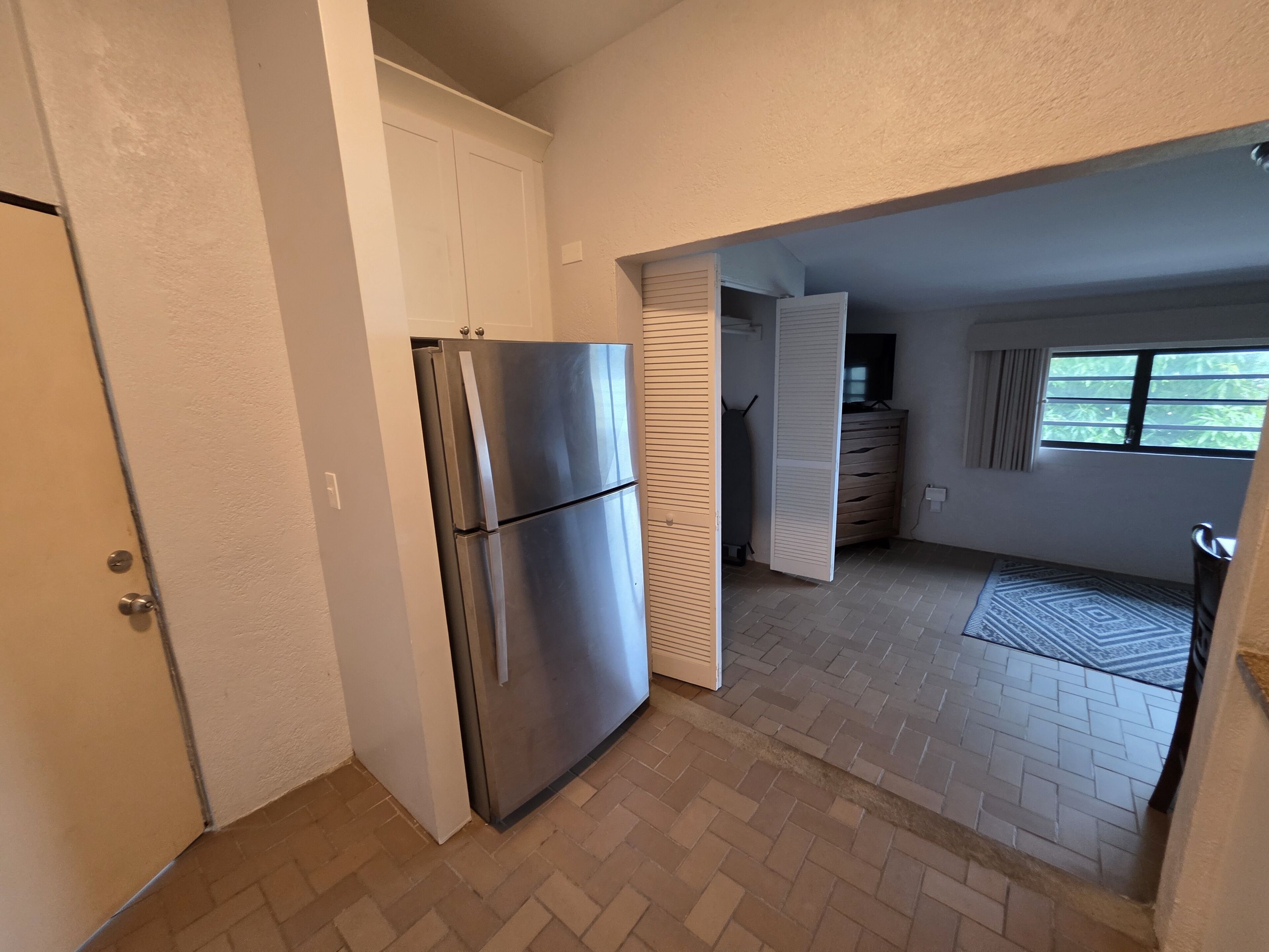 A compact kitchen with a stainless steel refrigerator, a wooden cabinet, and a window providing natural light.