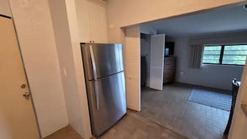 A compact kitchen with a stainless steel refrigerator, a wooden cabinet, and a window providing natural light.