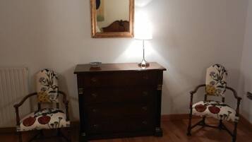 A room with two wooden chairs with floral upholstery, a dark wooden dresser with drawers, and a mirror on the wall.
