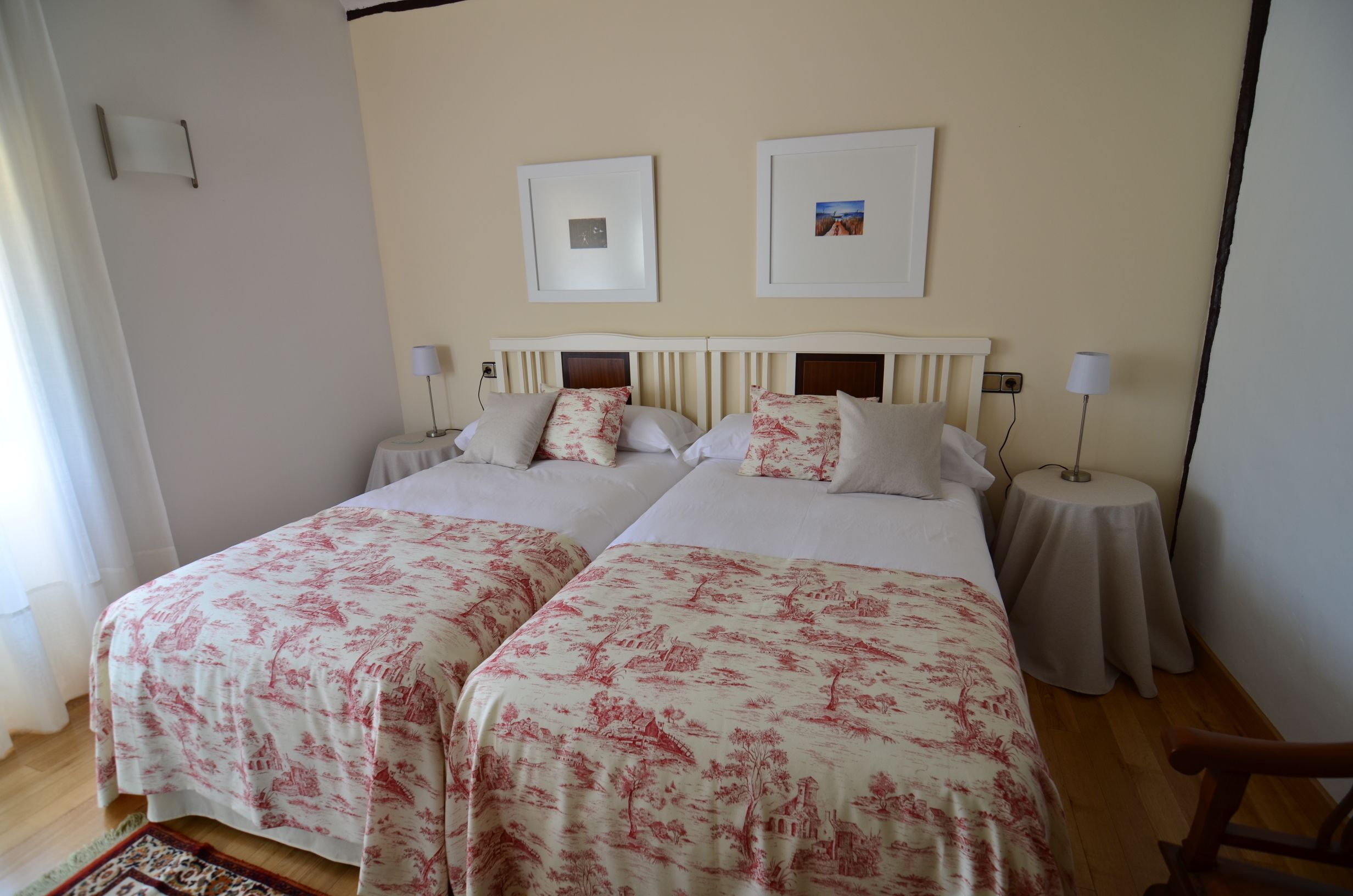 A double room with two beds, each with a floral bedspread, bedside tables with lamps, and framed pictures on the wall.