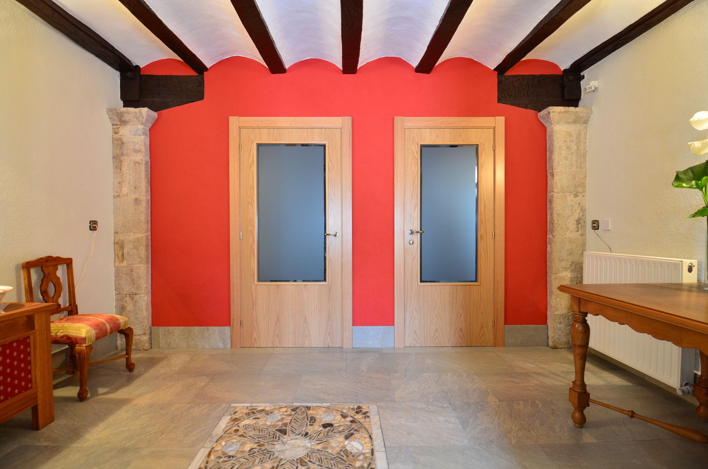 A room with two wooden doors with frosted glass panels, a wooden table, a chair, and a patterned rug.
