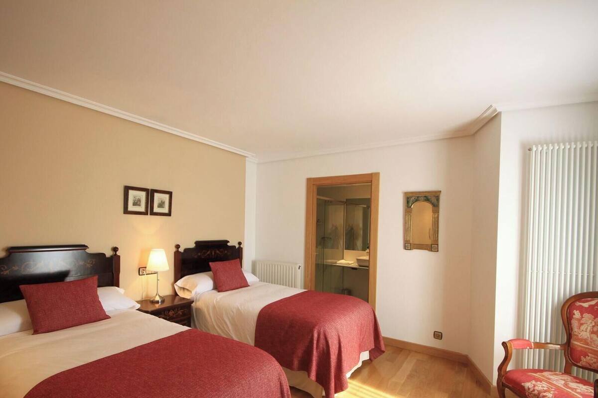 A hotel room with two beds, a wooden chair, a radiator, and a mirror on the wall.