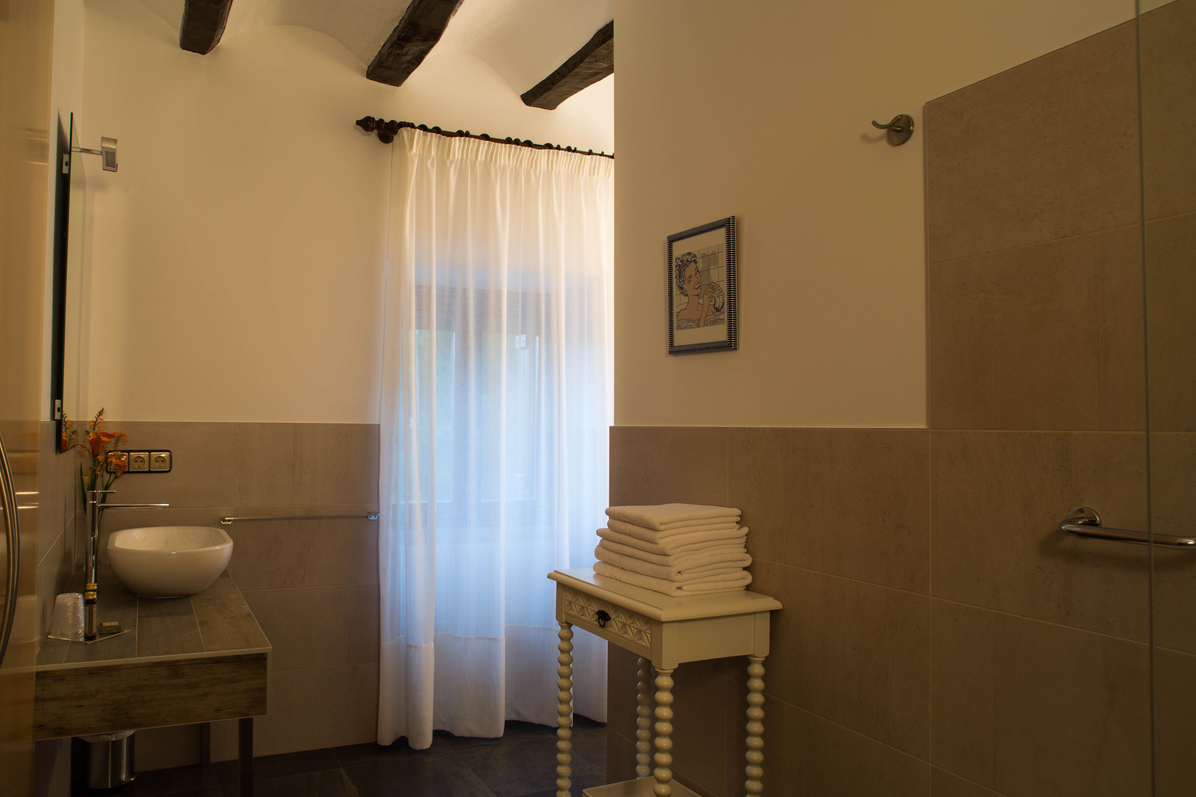 Un baño con lavabo, espejo, montón de toallas y cortina de ducha.