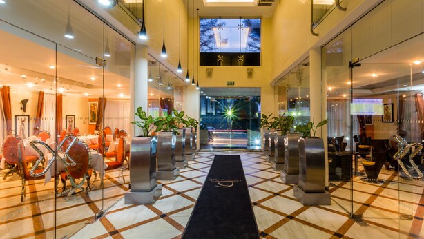 A hotel lobby with a checkered floor, a black carpet leading to the exit, and glass walls on either side. - Morning Side Suites (Lagos)
