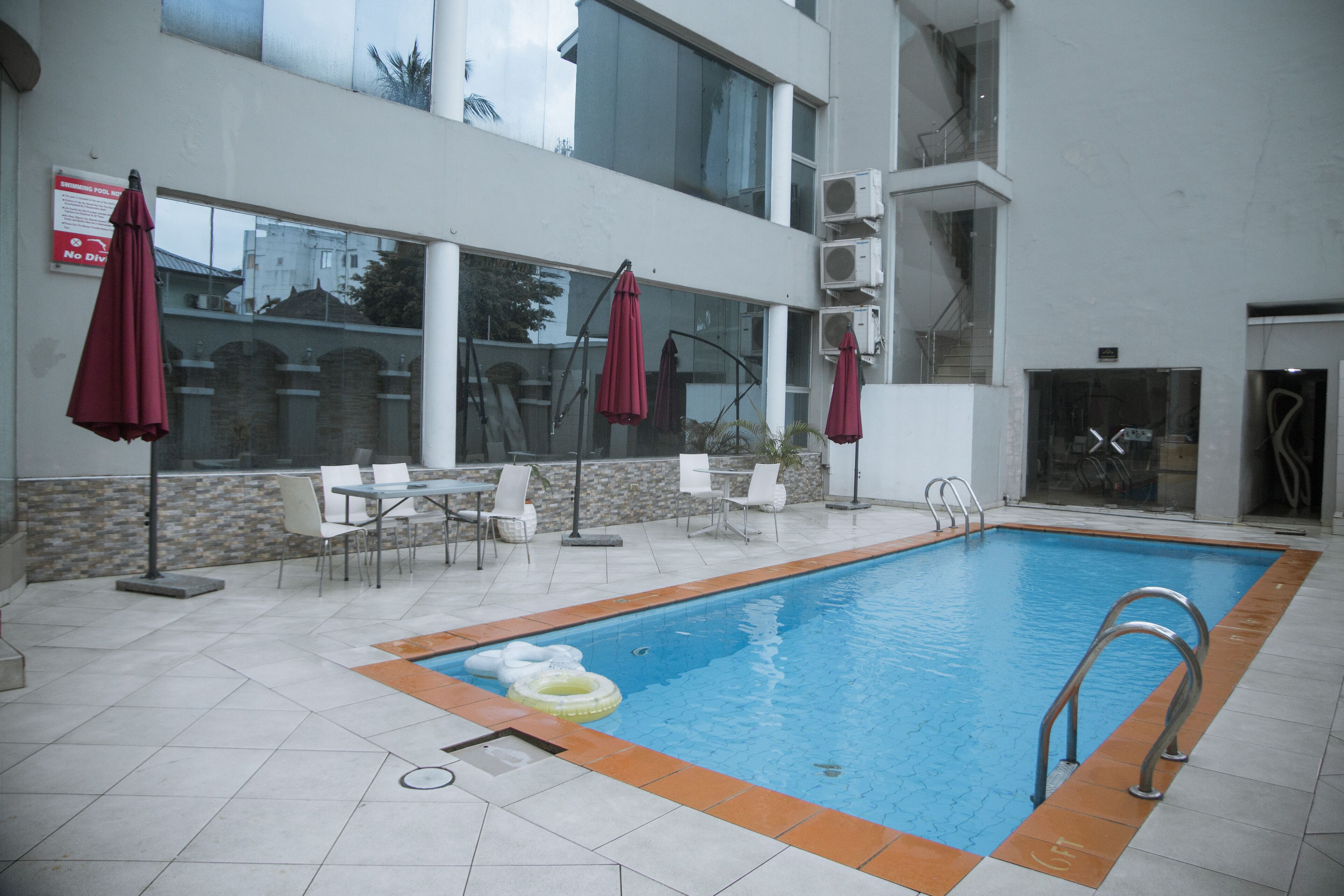 Une piscine intérieure avec un sol carrelé, entourée de chaises et de tables blanches, et de parasols rouges.