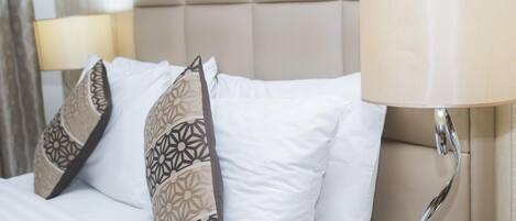 A neatly made bed with white linens and patterned pillows, a beige headboard, and a bedside lamp.