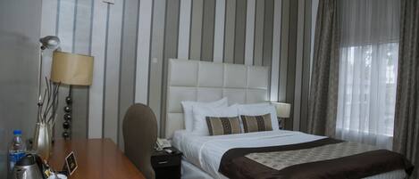 A hotel room with a large bed, a desk with a lamp, a telephone, and a coffee maker.
