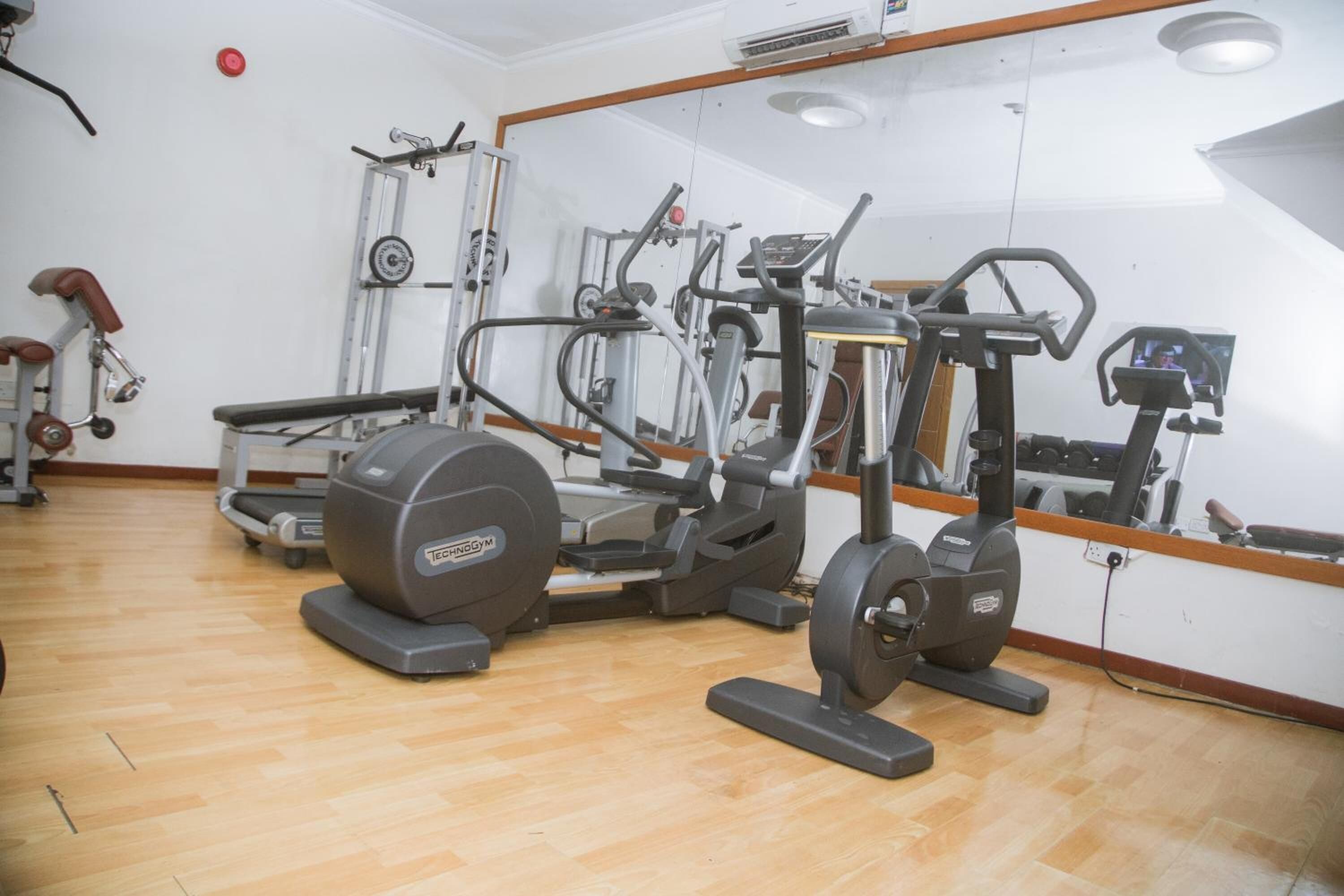 A gym with various exercise machines, a mirrored wall, and wooden flooring.
