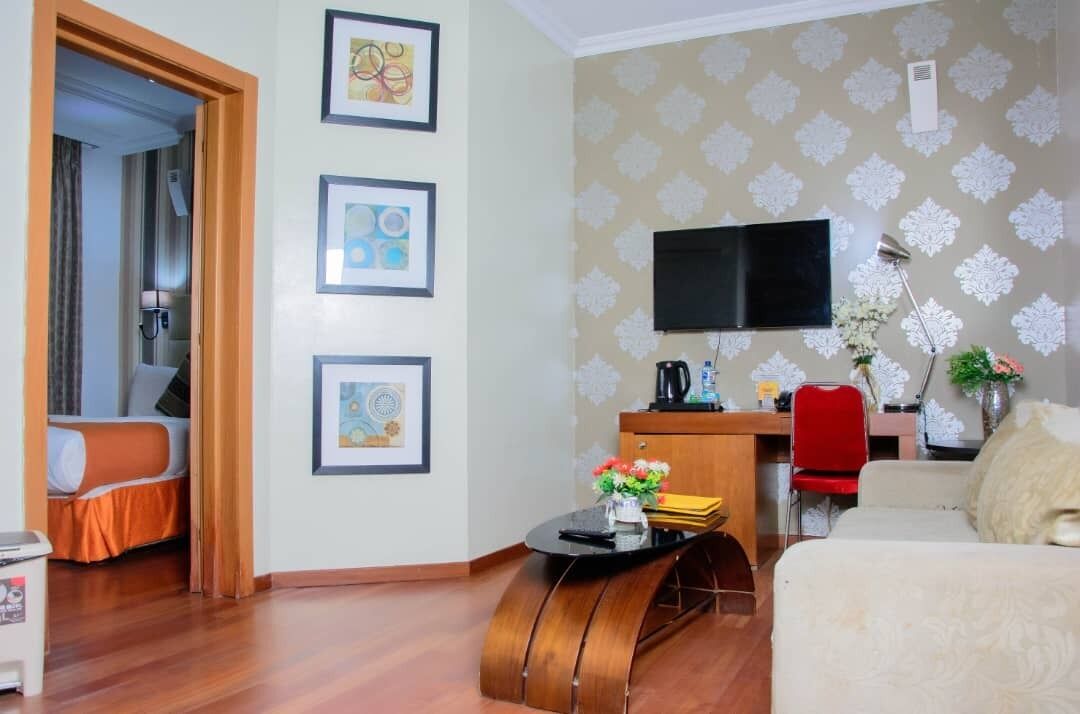 Habitación de hotel con cama, escritorio con computadora, televisión montada en la pared y obras de arte enmarcadas.