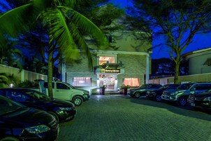 Un hotel con camino de entrada pavimentado, coches estacionados y palmeras.