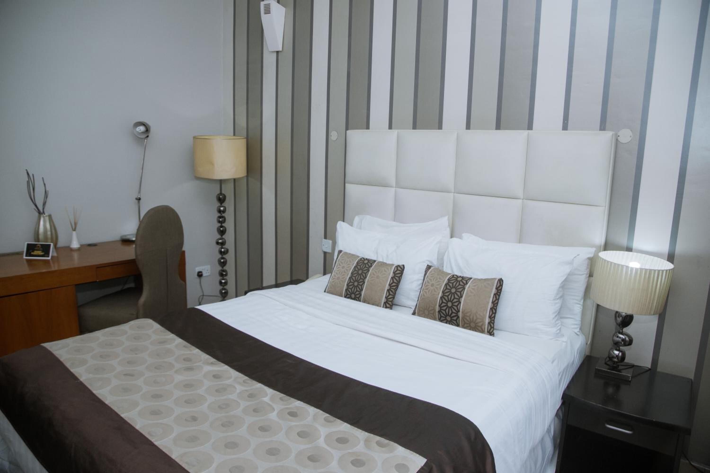 A hotel room with a large bed, a desk, a chair, a lamp, and a wall-mounted air conditioner.