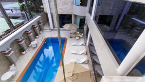 A rooftop pool area with a long rectangular pool, lounge chairs, and a small table with an umbrella. - Morning Side Suites (Lagos)