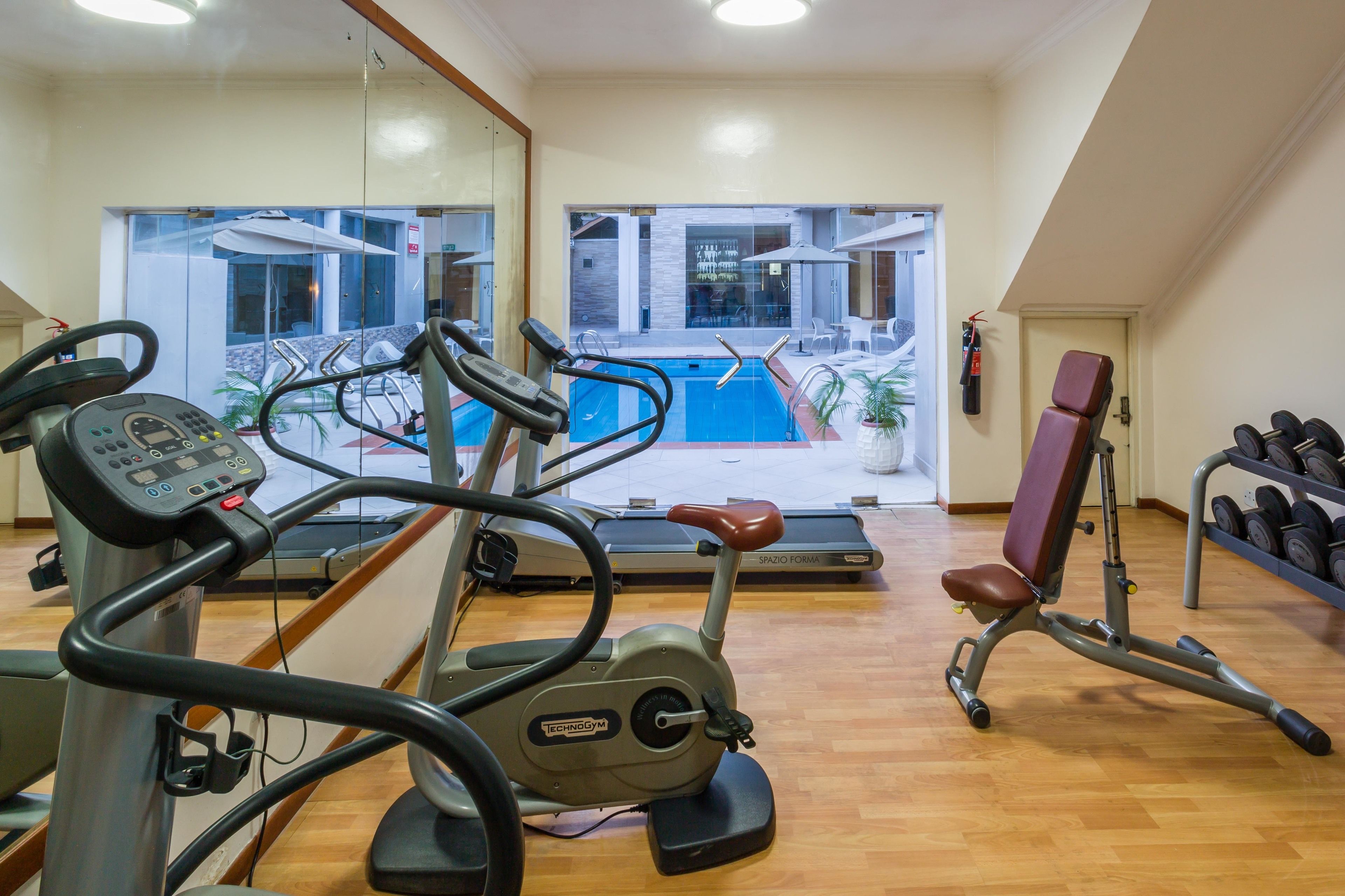 A gym with cardio equipment, a bench press, and a rack of dumbbells.
