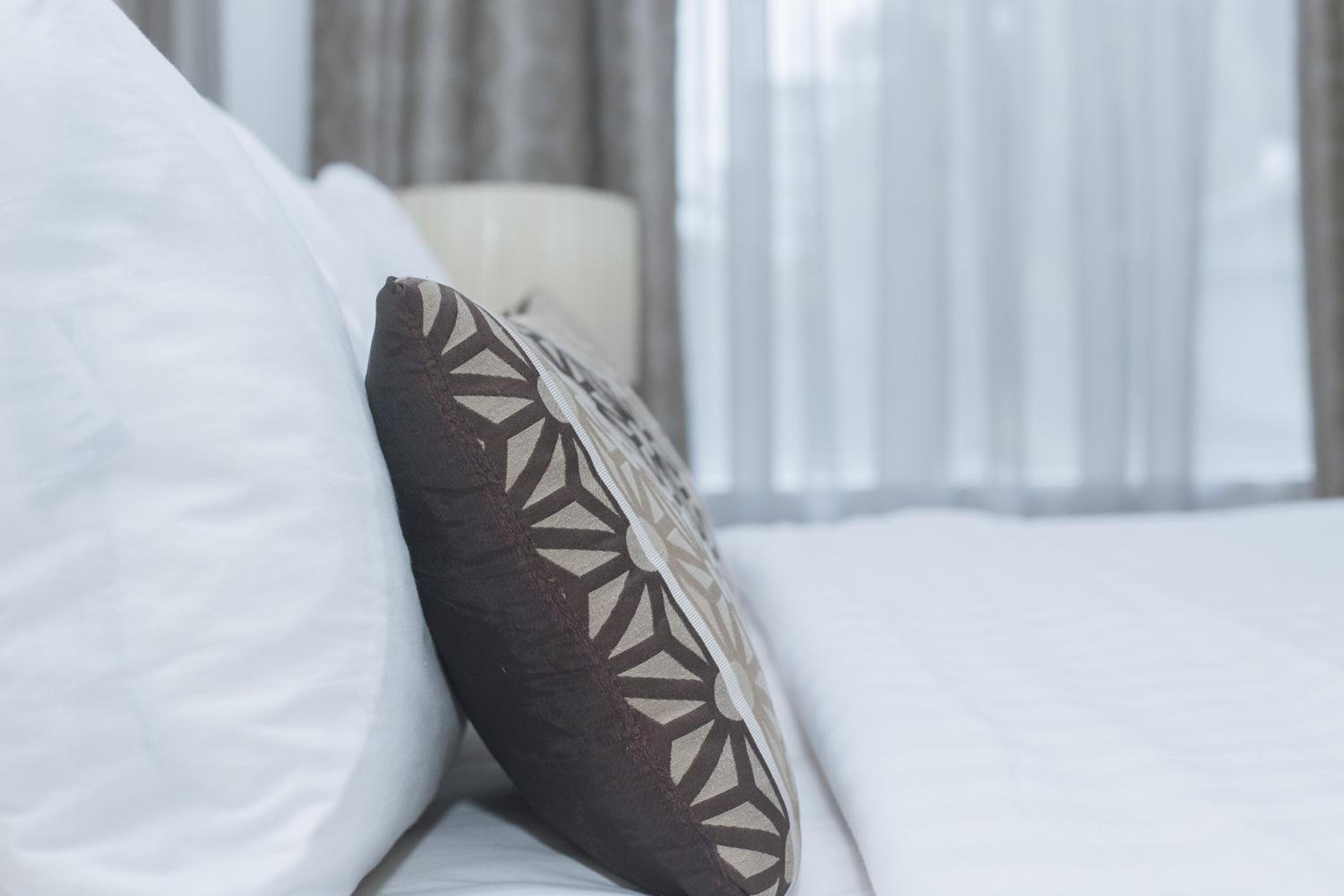A bed with white bedding and a patterned pillow.