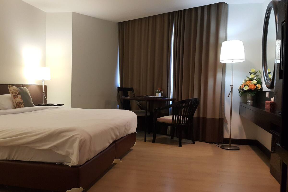 A hotel room with a large bed, a desk with a chair, a desk lamp, and a mirror.