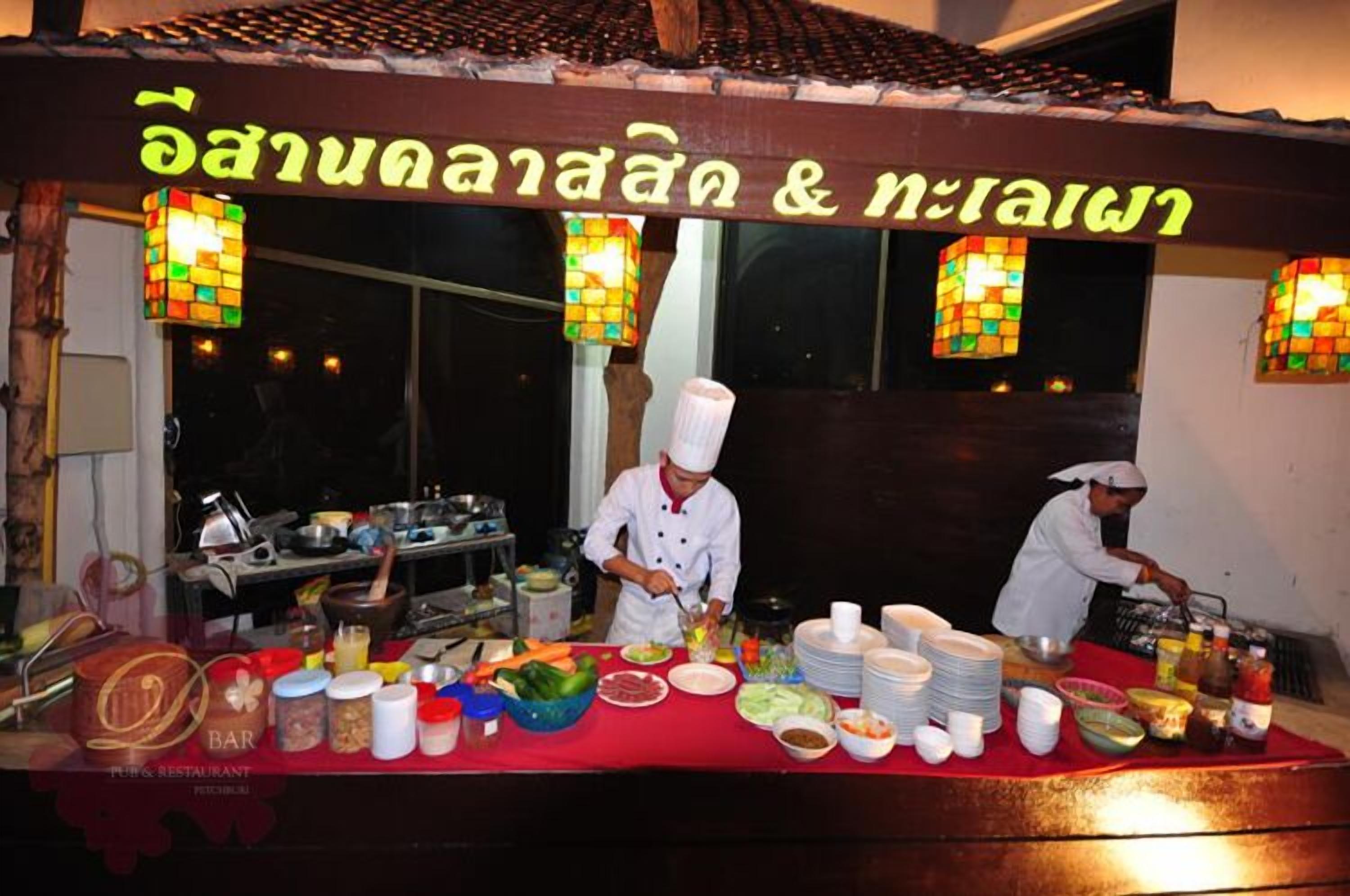 A food stall with a sign in a foreign language, a chef preparing food, and various food items and utensils on display.