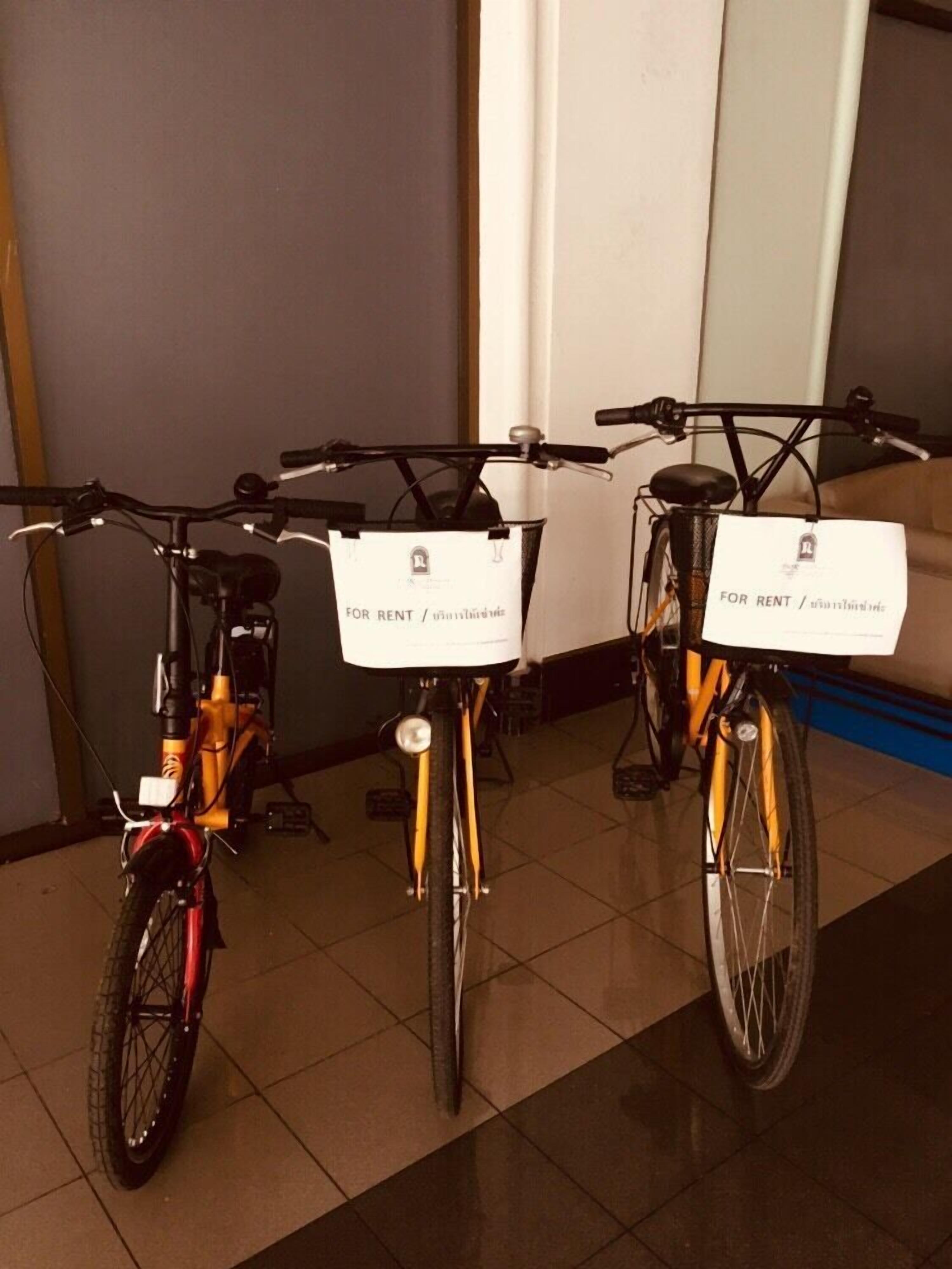Three bicycles with rental tags in a room with tiled flooring and a sofa in the background.