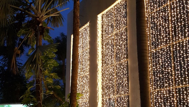 A building with vertical light strings and palm trees. - Royal Diamond Hotel (Phetchaburi)