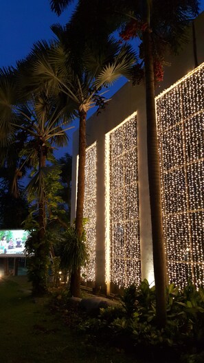 A building with vertical light strings and palm trees. - Royal Diamond Hotel (Phetchaburi)