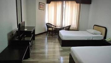 Habitación de hotel con dos camas individuales, un escritorio con silla, una mesita y una ventana con cortinas.