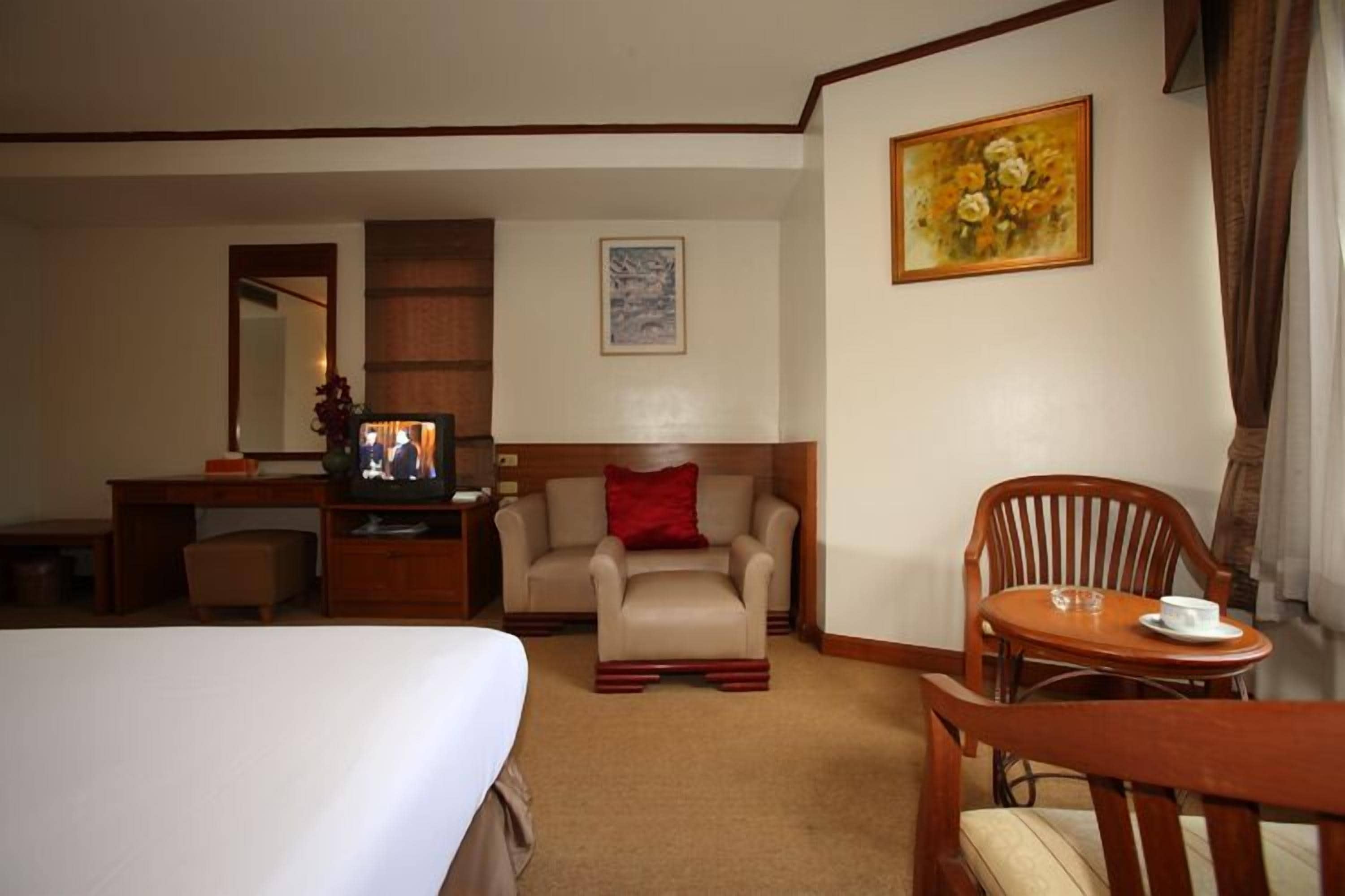 A hotel room with a bed, a desk with a television, a sofa, a chair, and a table with a cup.