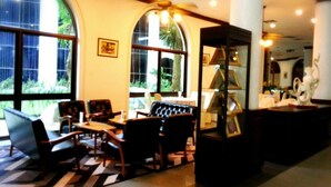 A spacious lobby with large windows, a seating area with leather chairs, and a display cabinet with framed pictures. - Royal Diamond Hotel (Phetchaburi)