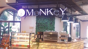 A Monkey-themed café with a glass display case, a coffee machine, and a wall-mounted plant. - Royal Diamond Hotel (Phetchaburi)