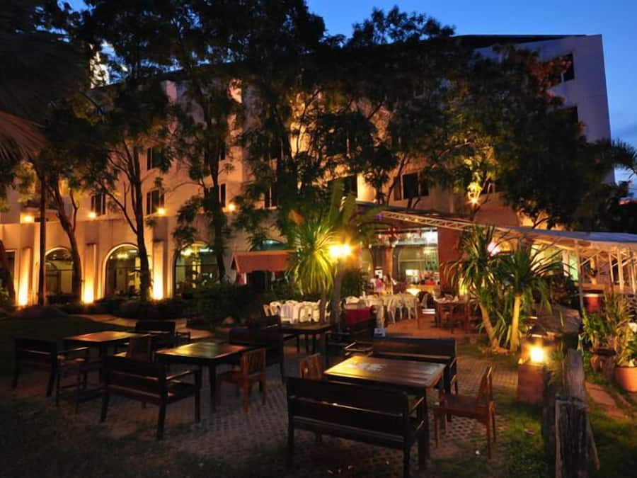 An outdoor dining area with tables and chairs, surrounded by trees and a building with illuminated windows.