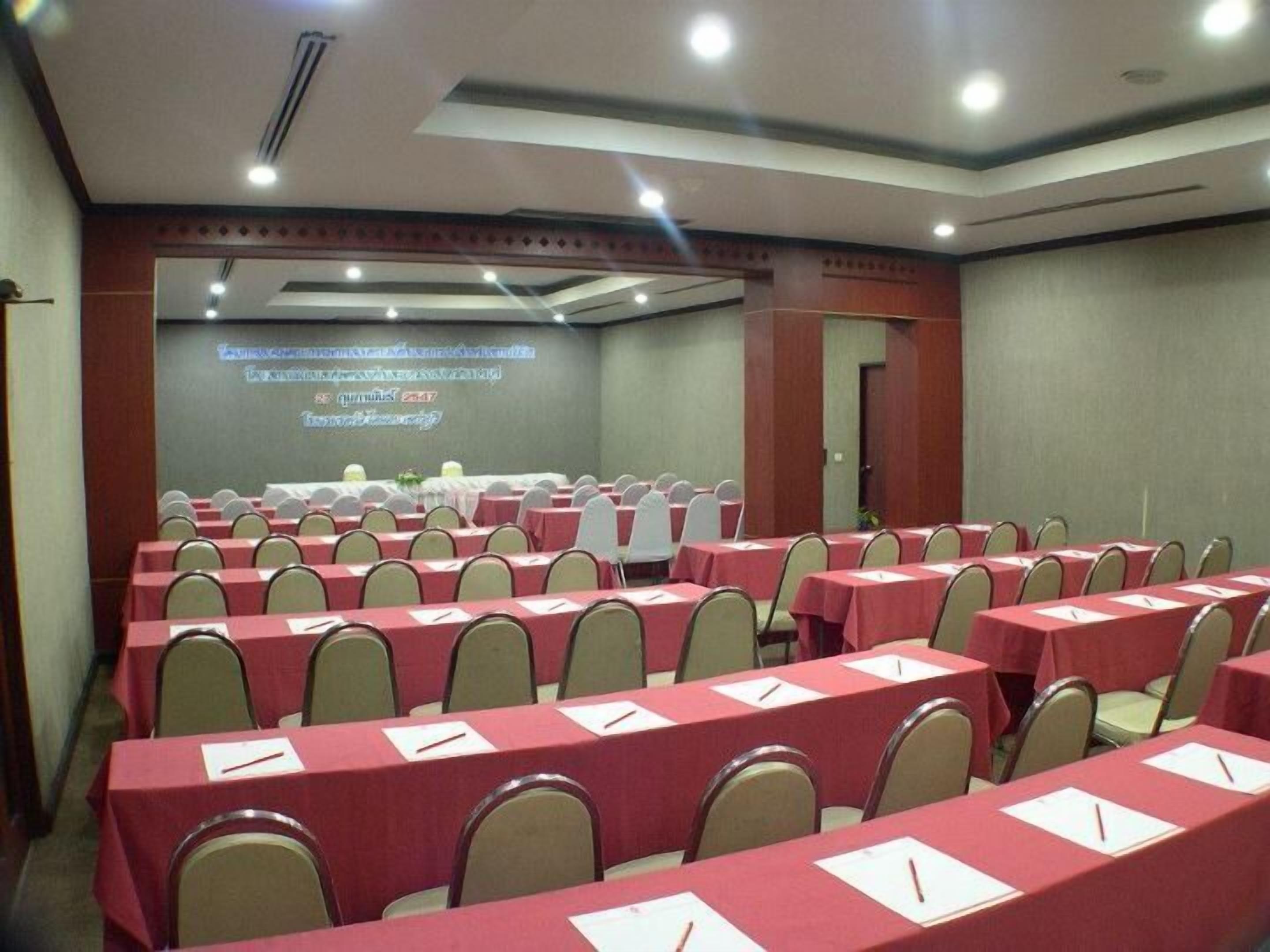Un salón de conferencias con filas de mesas y sillas, una pantalla de proyección y una puerta.