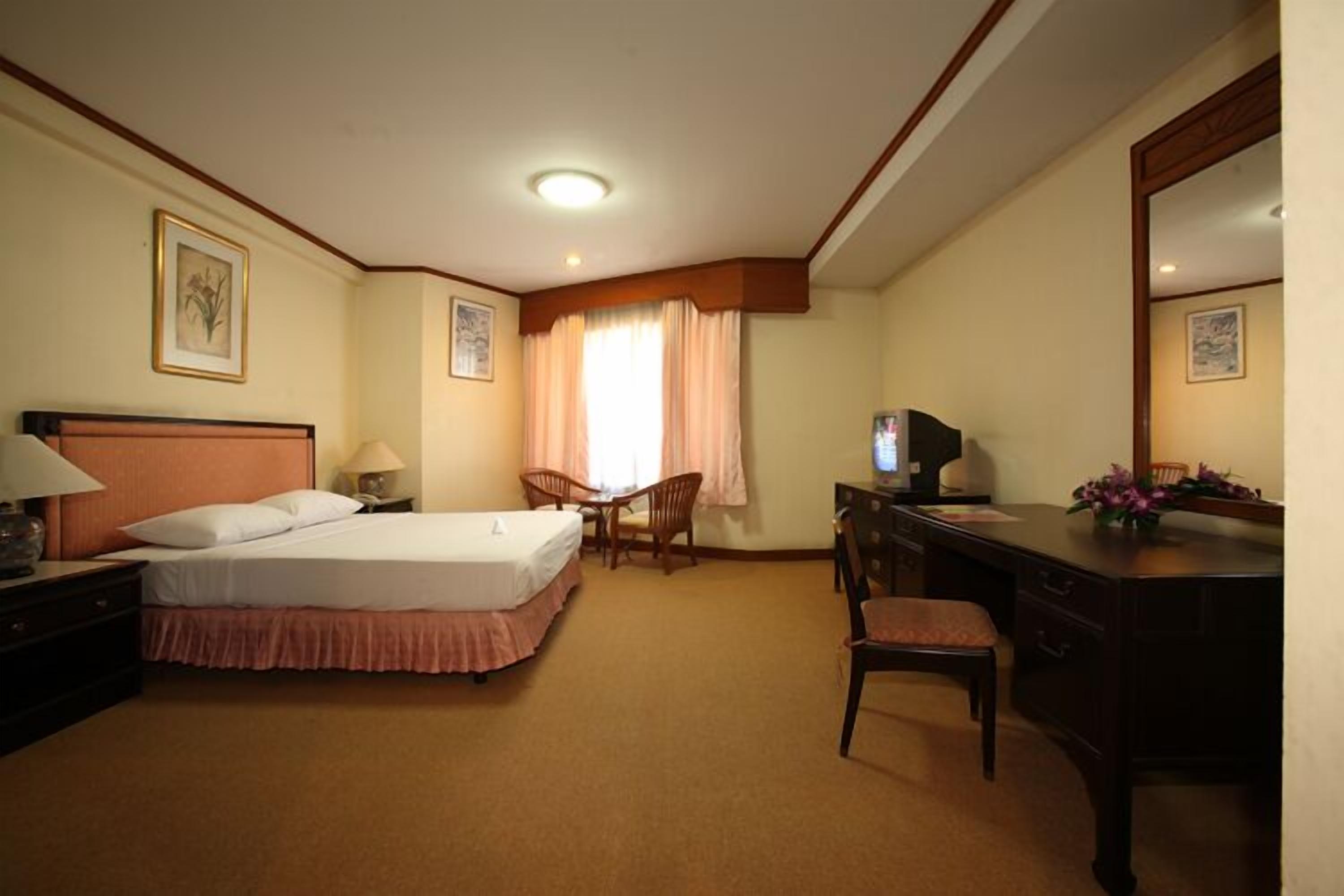 A hotel room with a bed, desk, chair, and a television.