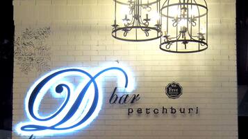 En musiker uppträder på scenen med en neonreklamskylt som visar texten ”D bar petchburi” och en Wi-Fi-symbol.