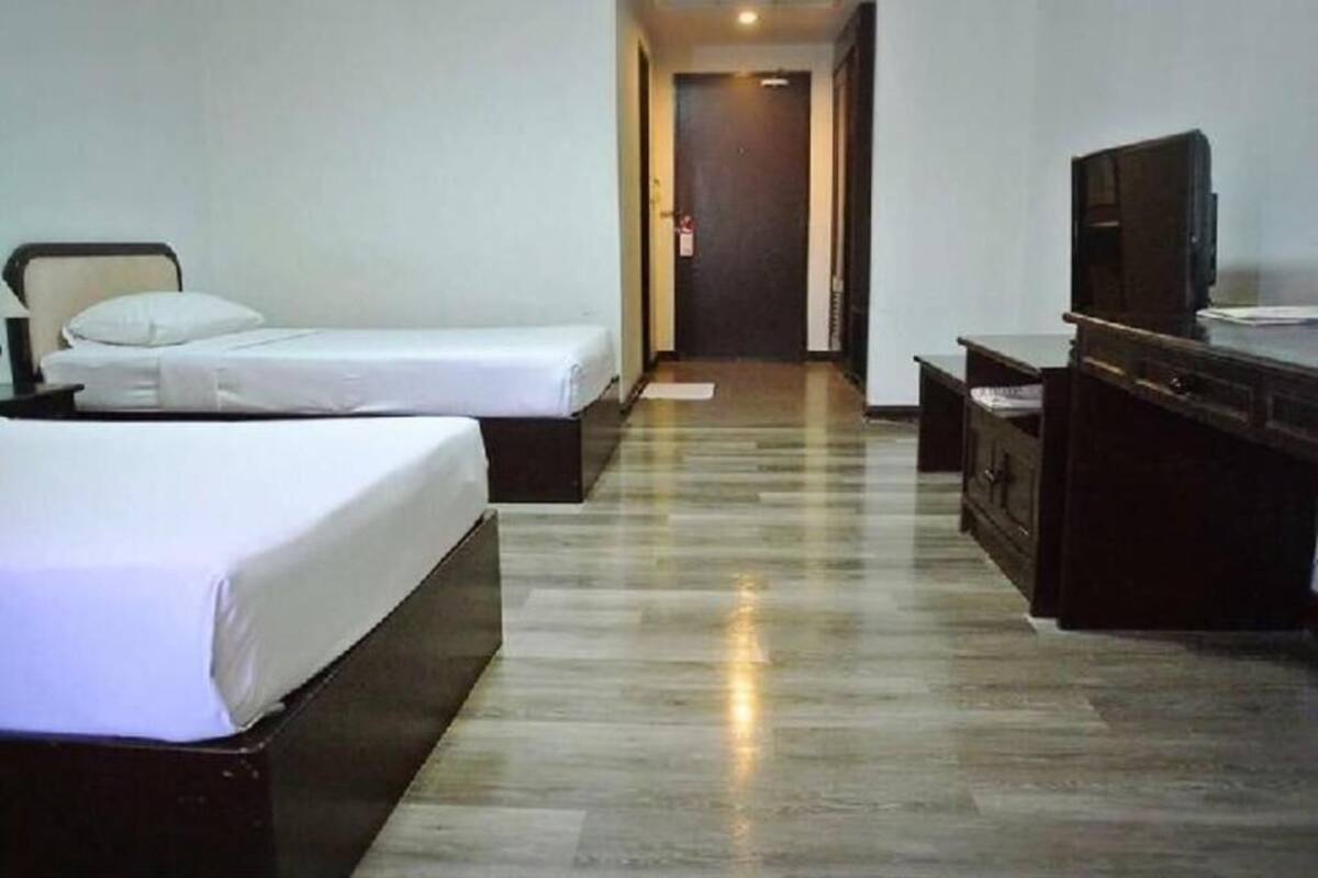 A hotel room with two single beds, a desk with a chair, a television, and a door in the background.