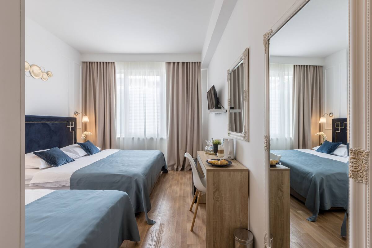 A hotel room with two beds, a desk, a mirror, and a window with curtains.