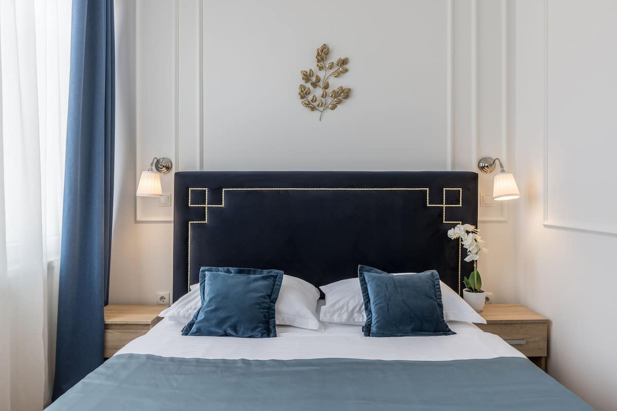 A neatly made bed with a dark headboard, two bedside lamps, and a decorative wall piece.