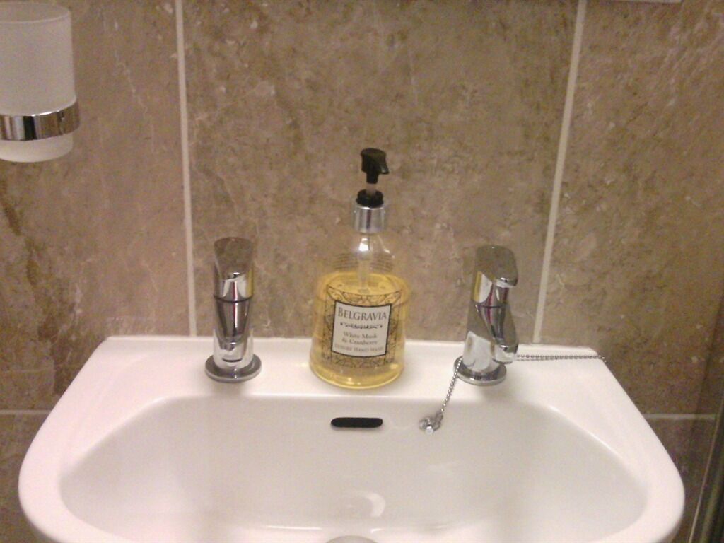 A bathroom sink with a bottle of Belgravia cologne and two faucets.