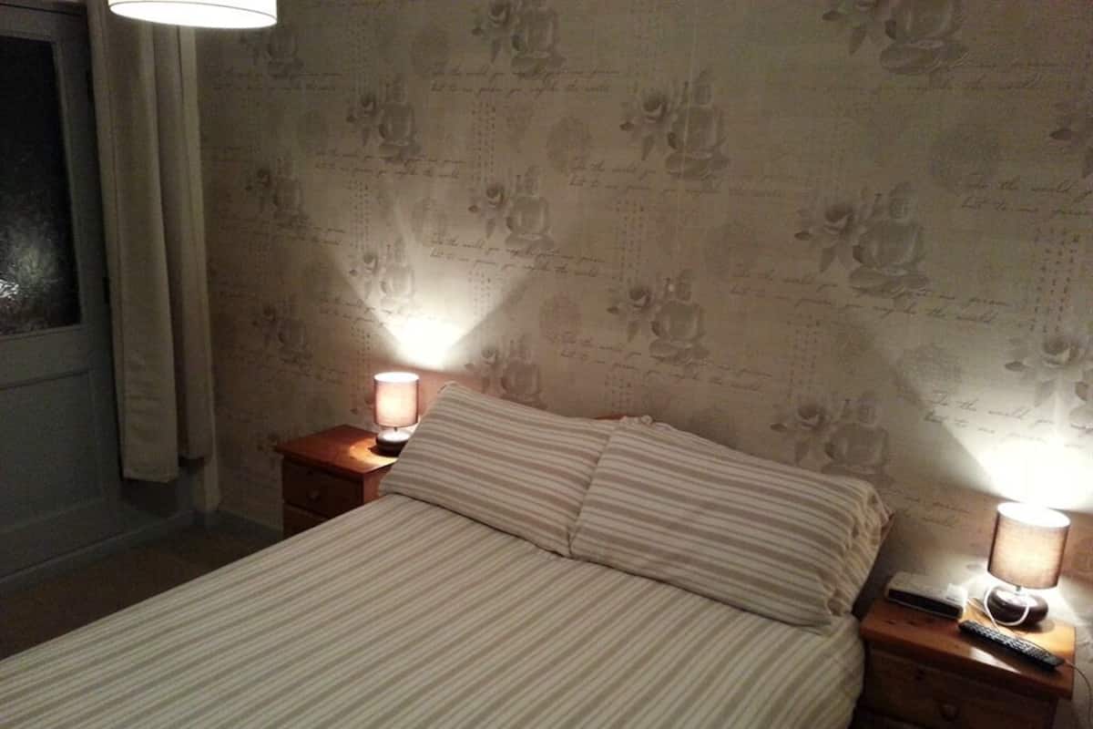 Una cama con ropa de cama a rayas, dos lámparas de noche, una mesita de noche y una pared con estampado floral.