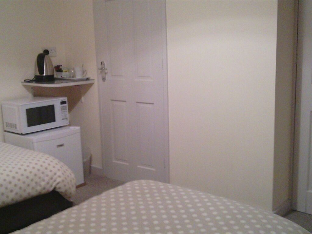 A bedroom with two beds, a microwave, a small cabinet, and a white door.