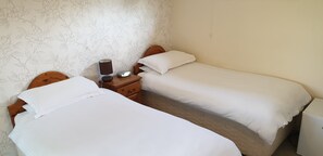 Two single beds with wooden headboards, a nightstand with a lamp and a small appliance, and floral wallpaper. - Beoley Lodge (Redditch)