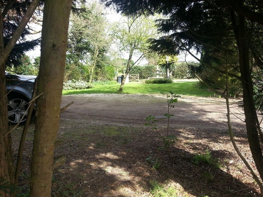 Un aparcamiento con un sendero de tierra que conduce a una puerta, rodeado de árboles y vegetación.