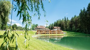 A large, multi-story building with a reflective pool in front, surrounded by lush greenery and trees. - Green Lake Hotel Weiher (Pfalzen)