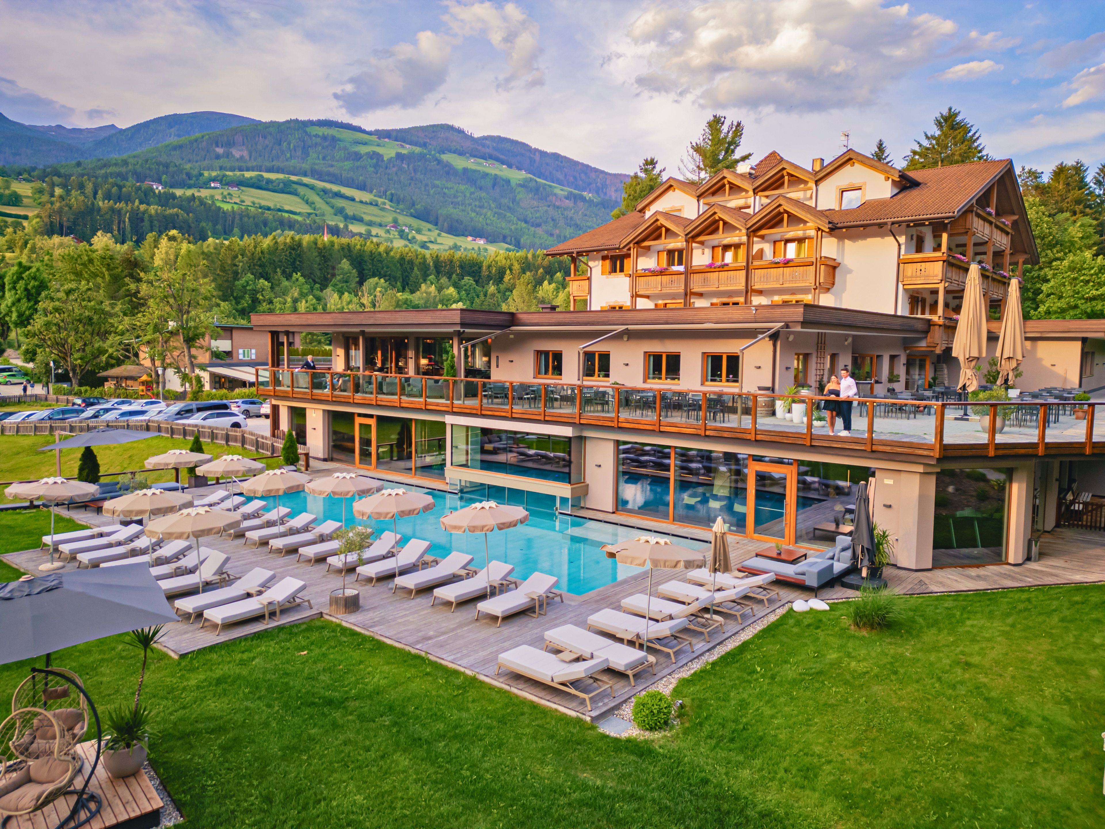 Un albergo con piscina, lettini e vista sulle montagne.