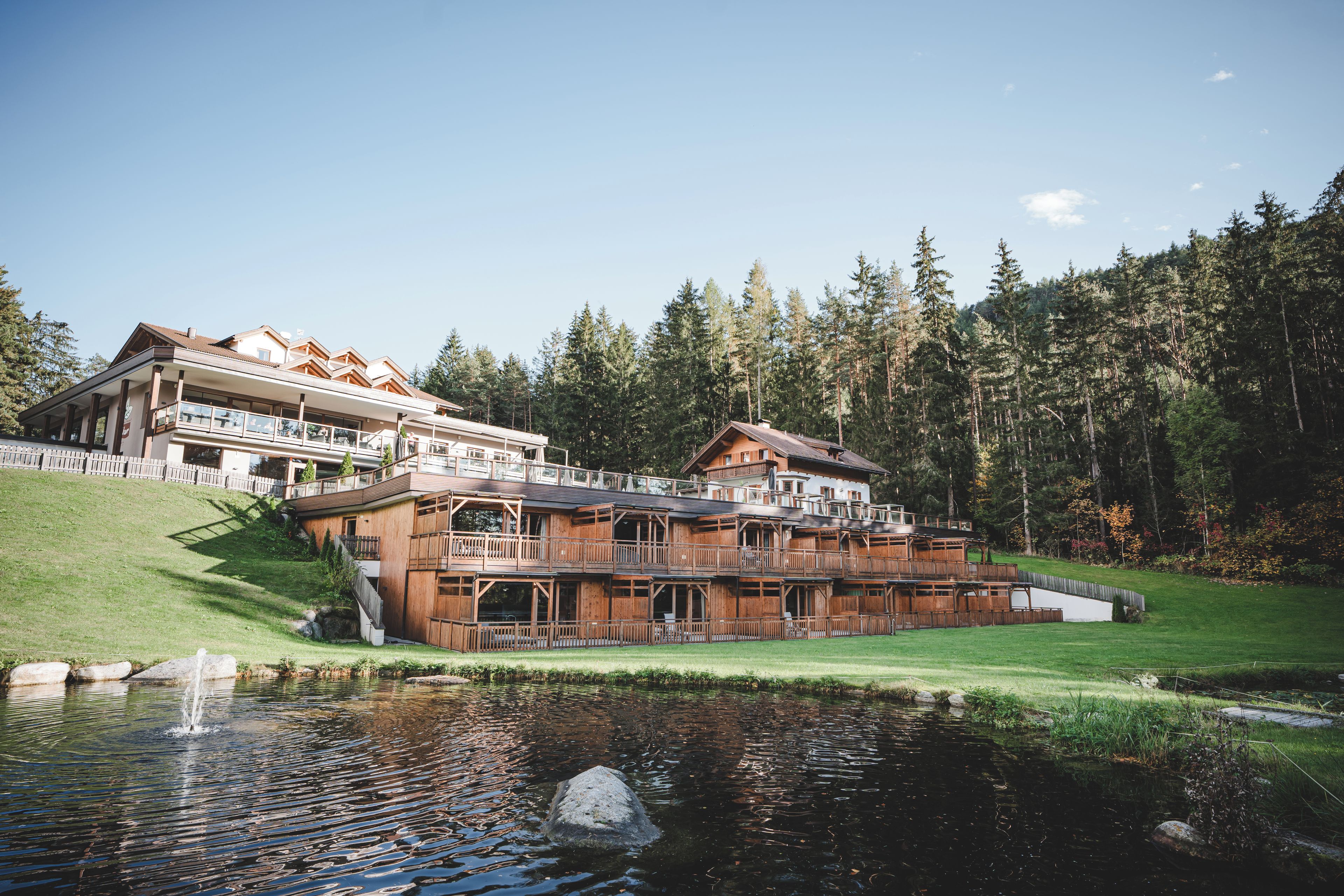A large wooden lodge with multiple balconies and a pond in front.