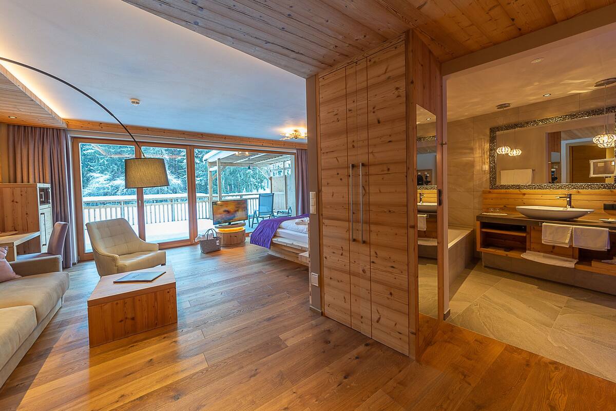 Un interior moderno con piso de madera, un sofá, un televisor y un baño con un espejo grande y lavamanos.
