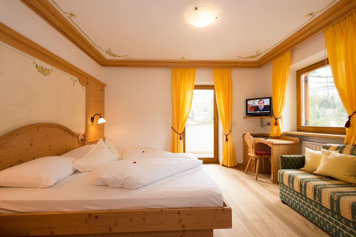 Habitación de hotel con una cama y un escritorio de madera, un sofá verde y un televisor sobre el escritorio.