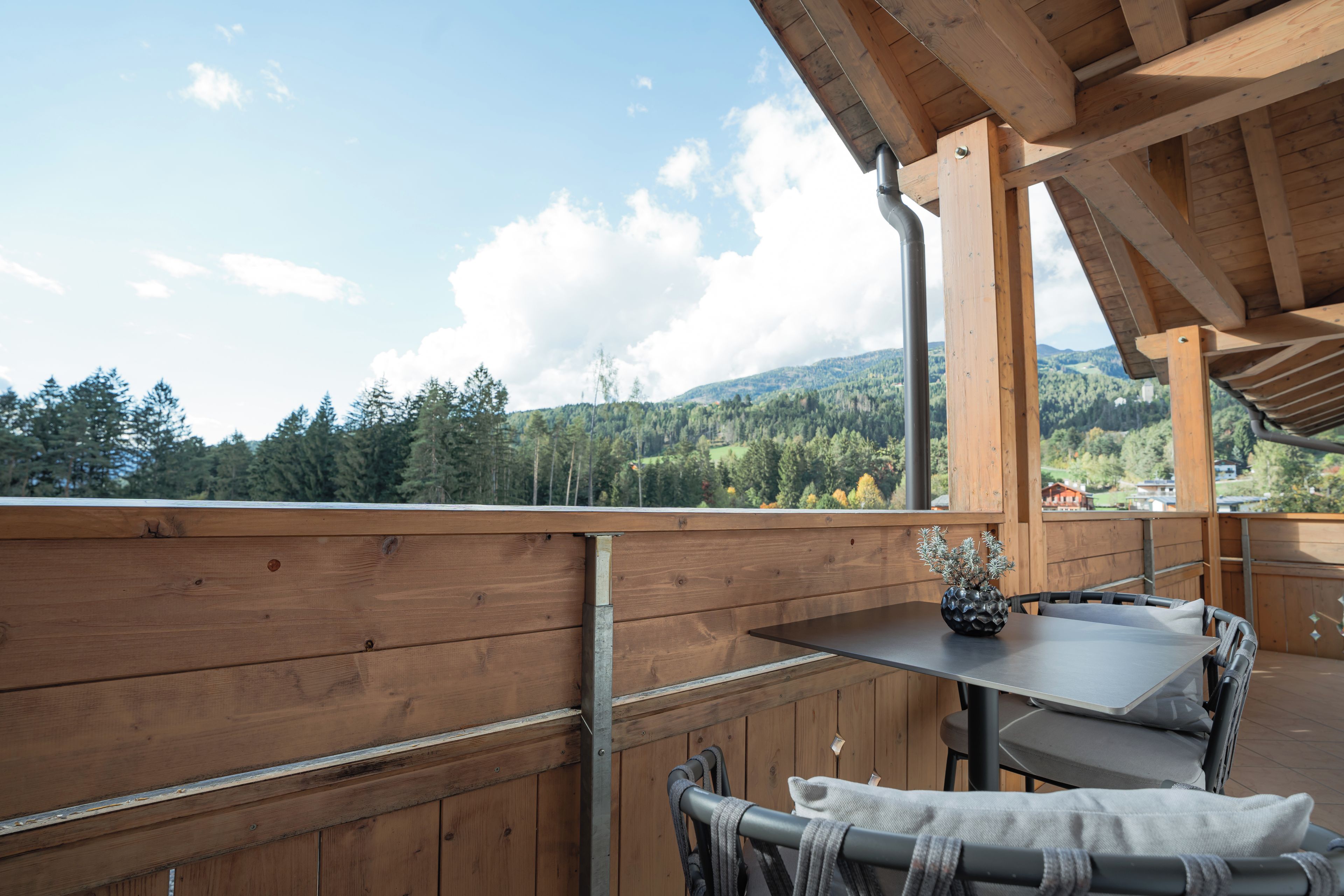 Terraza de madera con mesa y sillas, con vista a un valle boscoso.