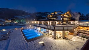 A modern hotel with a heated swimming pool, outdoor seating, and a view of snow-covered mountains. - Green Lake Hotel Weiher (Pfalzen)