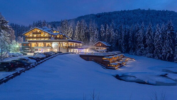 A large lodge with multiple guest rooms, a ski lift, and a snow-covered forest backdrop. - Green Lake Hotel Weiher (Pfalzen)