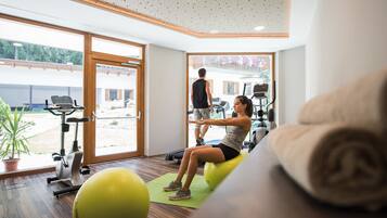 Une salle de sport équipée de matériel d’exercice, avec un grand ballon de gymnastique et une personne utilisant un appareil d’aviron.