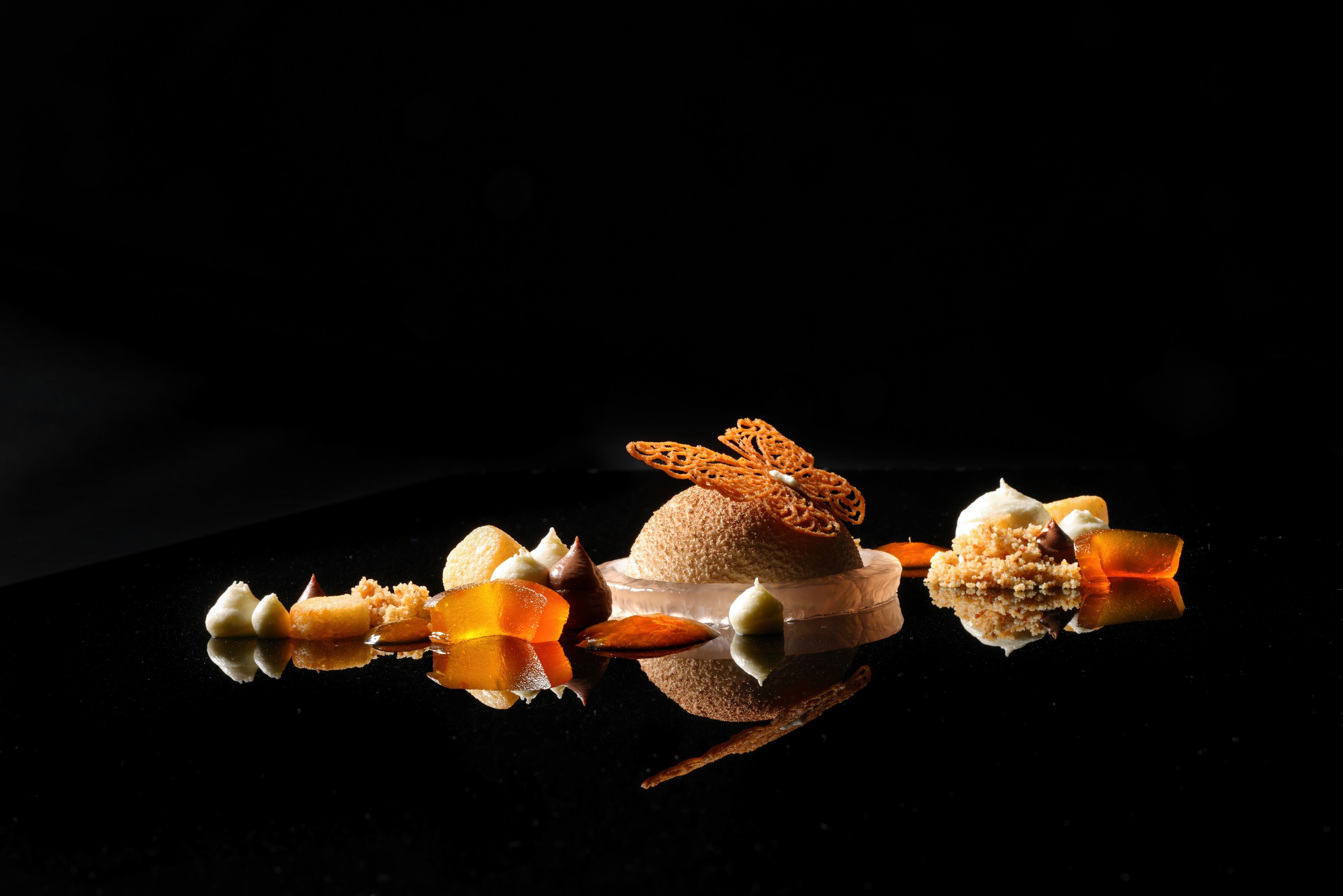 Un dessert composé de différents éléments, présenté sur une surface réfléchissante.